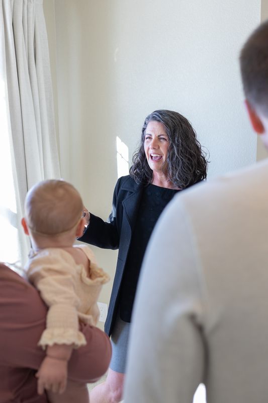 A real estate agent greeting a client family and reaching for their baby in a bright living room