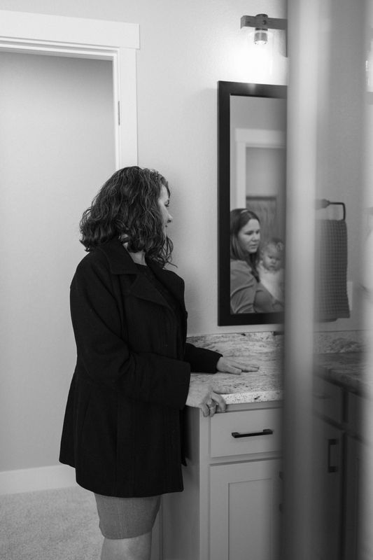 A real estate agent walking down a hallway, reflected in a bathroom mirror