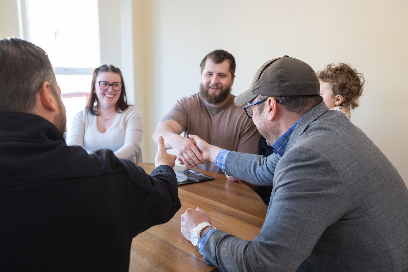 Four people meeting around a wooden table, two shaking hands over an open laptop
