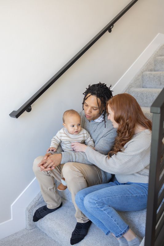 A couple sitting on the carpeted stairs of their home holding their baby between them