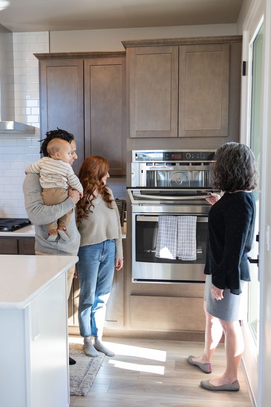 A mother holding her baby in a new kitchen while a real estate agent and a child look on