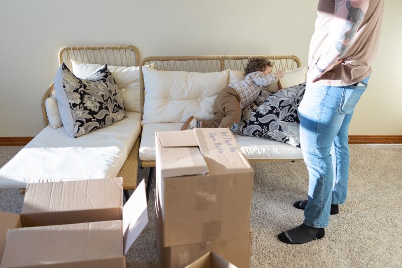 Open cardboard moving boxes in a living room while a parent and small child unpack behind them