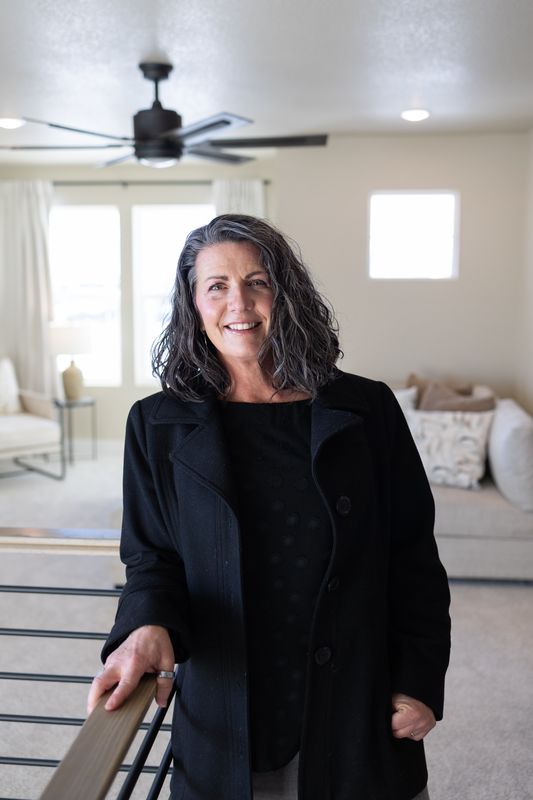 Portrait of realtor Nicole Strom standing in an empty living room in a black blazer
