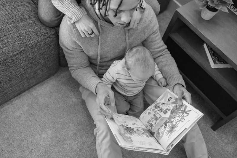 Overhead black and white photo of two parents holding an open picture book for a baby on their lap