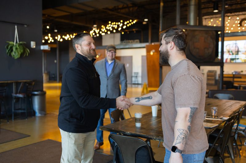 Three men meeting in a taproom, two shaking hands while a third looks on