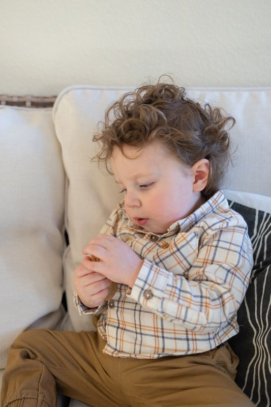 A curly haired toddler sitting quietly in a cream armchair looking down at his hands